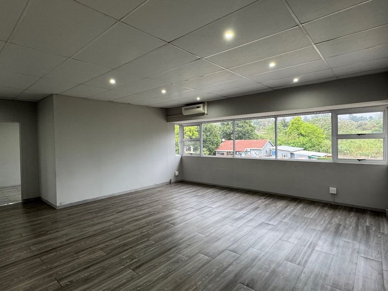 Spacious, empty living area featuring modern laminate flooring, a drop ceiling with recessed lighting, and large windows providing natural light and neighborhood views.