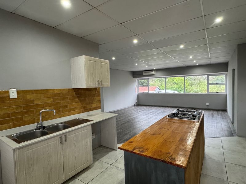 Spacious open-plan living area featuring a kitchen with a central island, gas hob, double sink, and neutral finishes, leading to a bright living space.