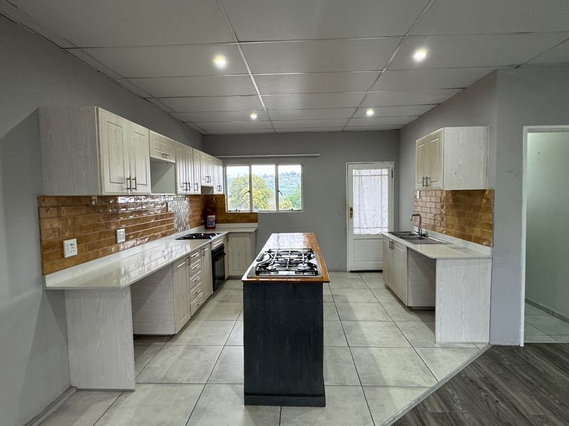 Spacious kitchen featuring a central island with gas hob, ample built-in cabinetry, tiled backsplash, and double sink, offering a functional layout for cooking.