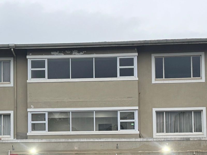 Exterior view of an apartment building facade featuring multiple aluminium-framed windows and visible signs of exterior paint deterioration.