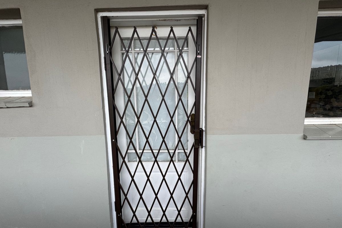 Exterior view of a rear door featuring a metal security gate and adjacent windows on a painted masonry wall.