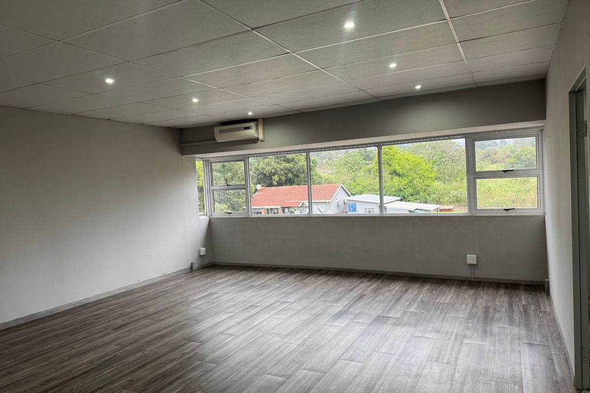 A bright, empty living area featuring modern laminate wood flooring, a drop ceiling with recessed lighting, and a large window with exterior views.
