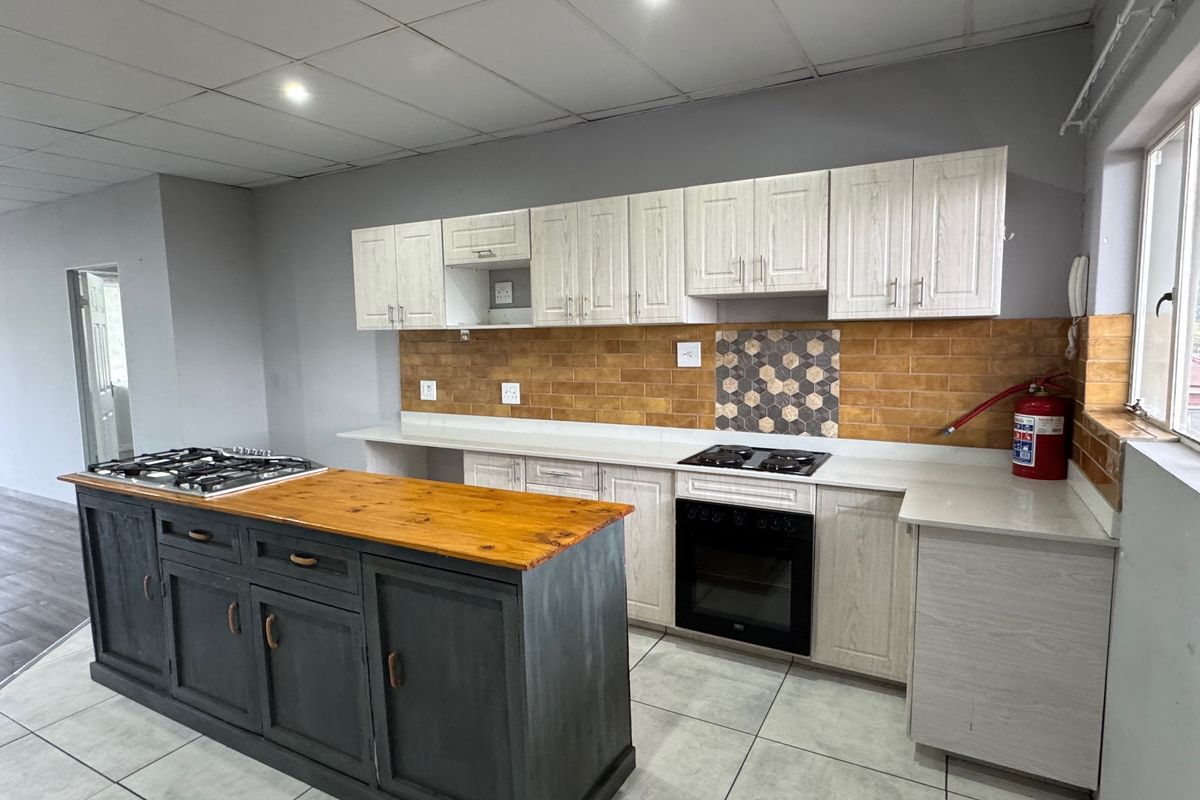 A spacious kitchen featuring a central island with a wooden countertop, built-in oven, gas hob, and ample cabinetry with a decorative tiled backsplash.