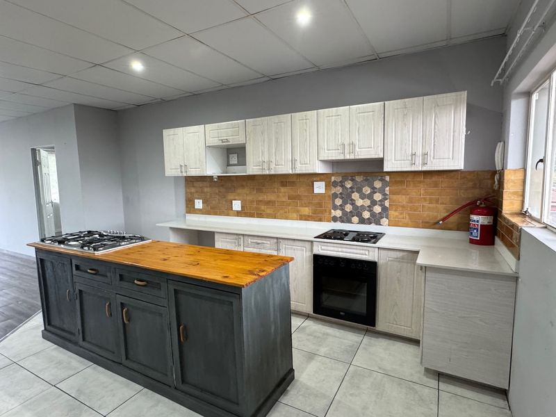 A spacious kitchen featuring a central island with a wooden countertop, built-in oven, gas hob, and ample cabinetry with a decorative tiled backsplash.