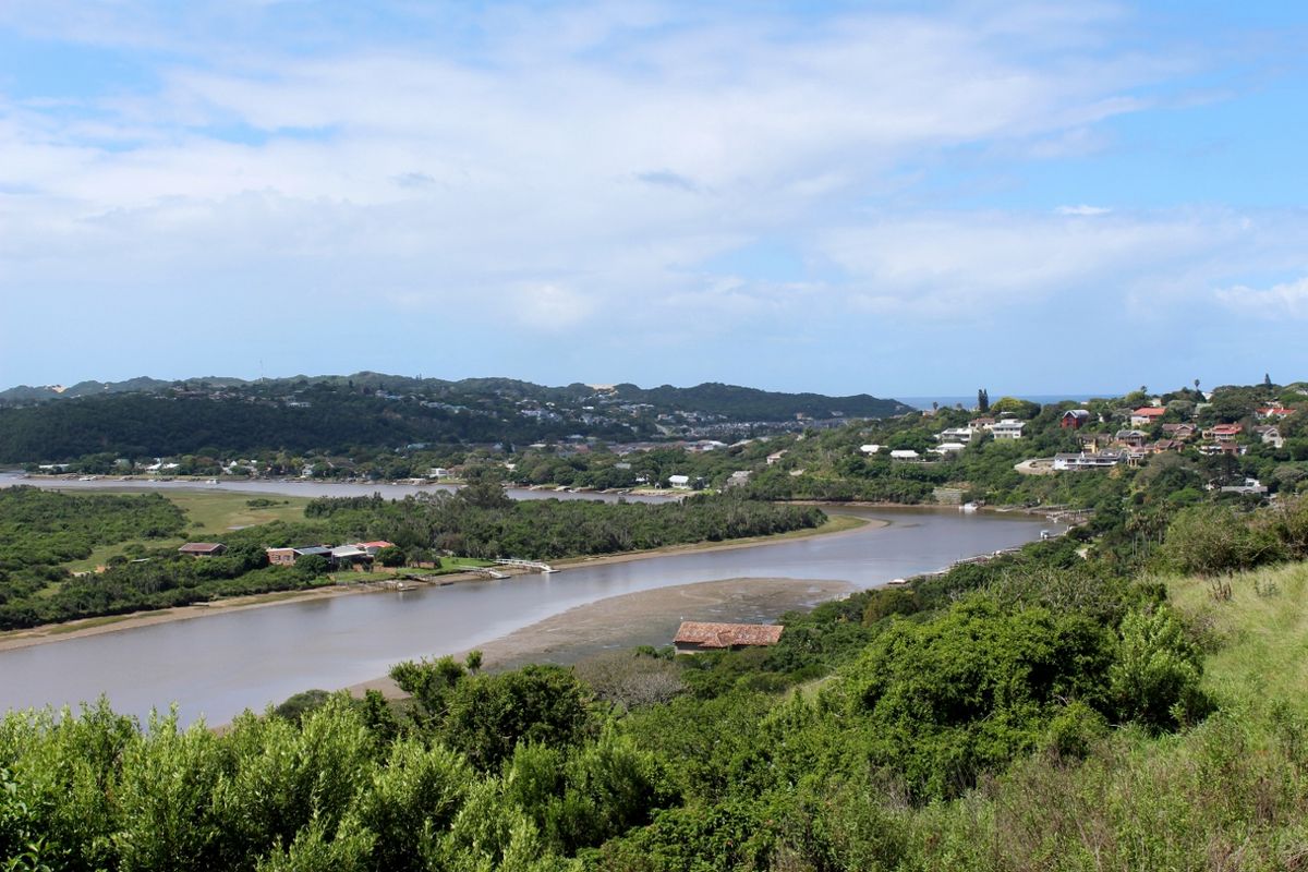 A scenic elevated view overlooking a river estuary, surrounding lush vegetation, and distant residential hillside developments.