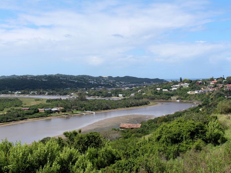 A scenic elevated view overlooking a river estuary, surrounding lush vegetation, and distant residential hillside developments.