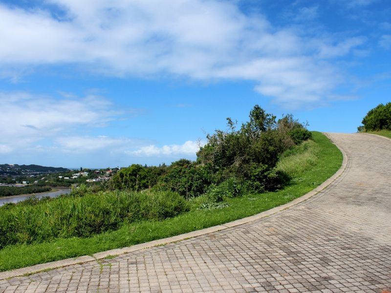 A paved driveway leading up a gentle slope, bordered by natural vegetation and offering scenic views of the surrounding landscape and river.