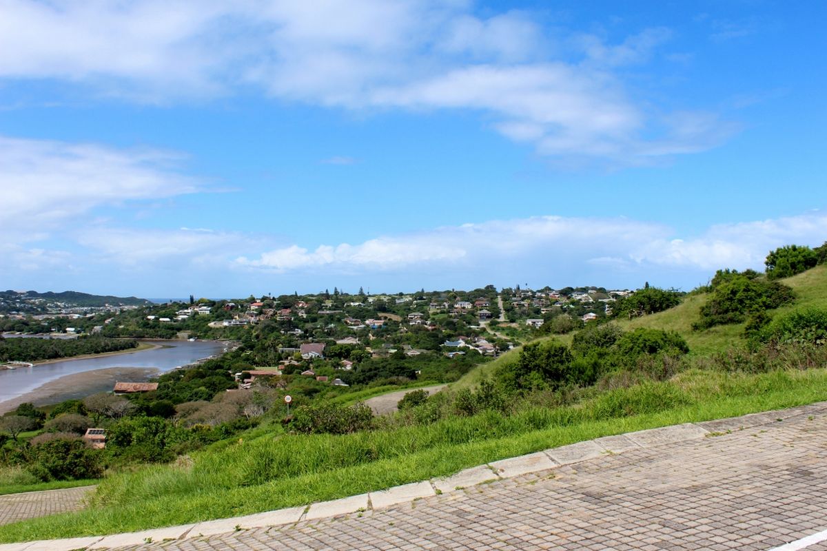 A scenic elevated view overlooking a coastal residential area, river estuary, and surrounding natural landscape from a paved street.