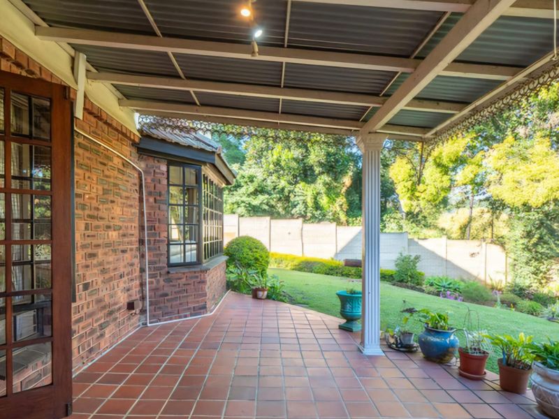 A covered patio area featuring tiled flooring, a brick facade, and a bay window, overlooking a private garden space.