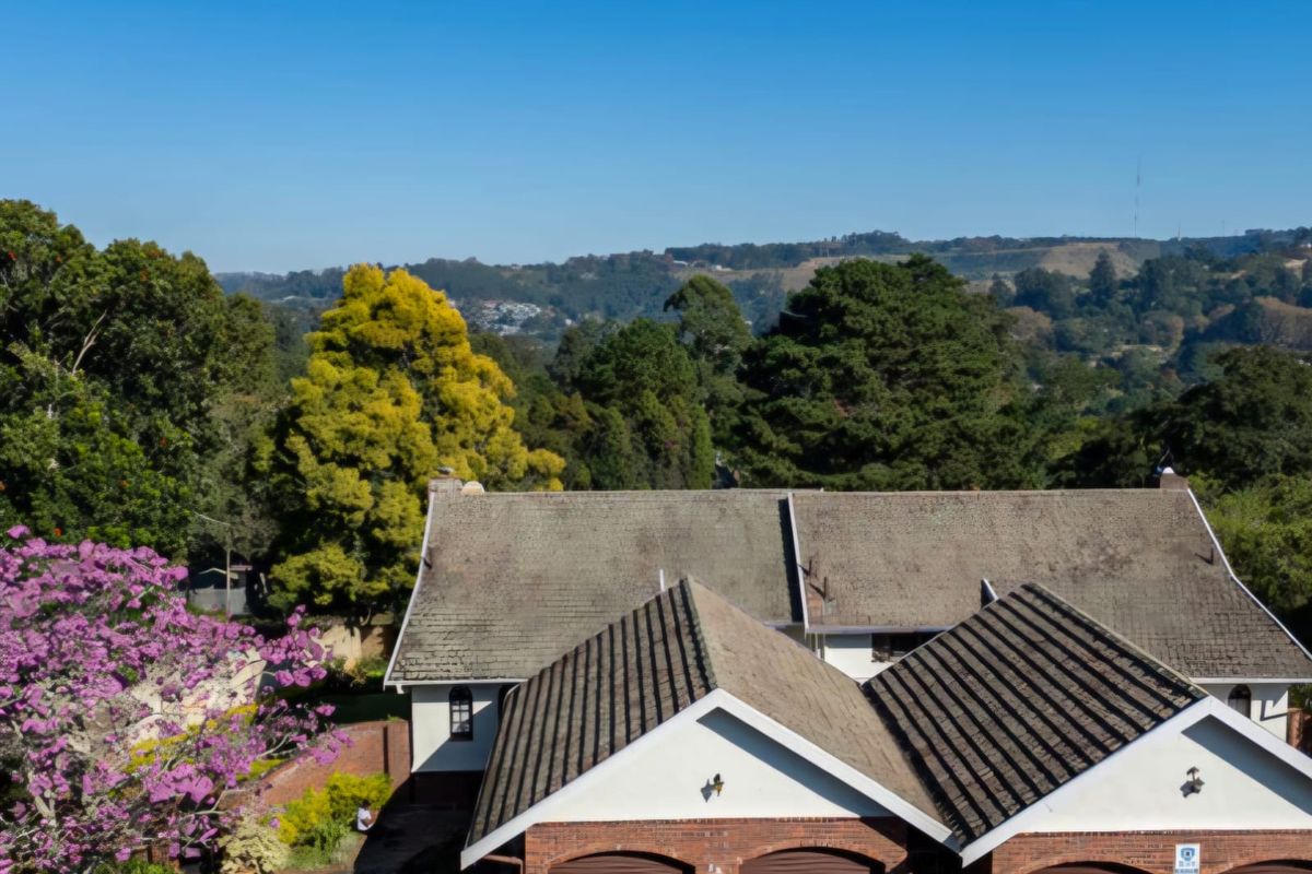 Aerial view of a townhouse complex featuring a multi-car garage, tiled roofing, and established garden surroundings with scenic landscape views.