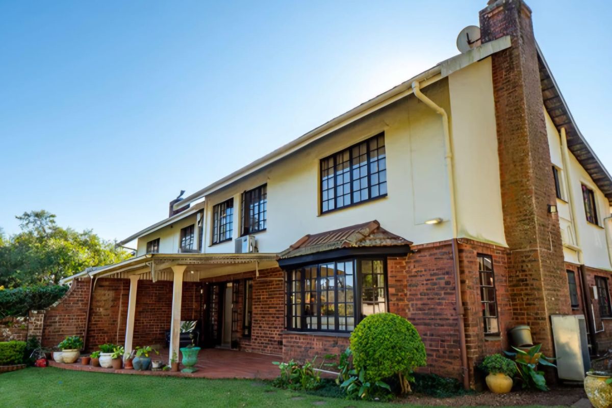 Rear view of the townhouse featuring a brick facade, covered patio area, bay window, and established garden.