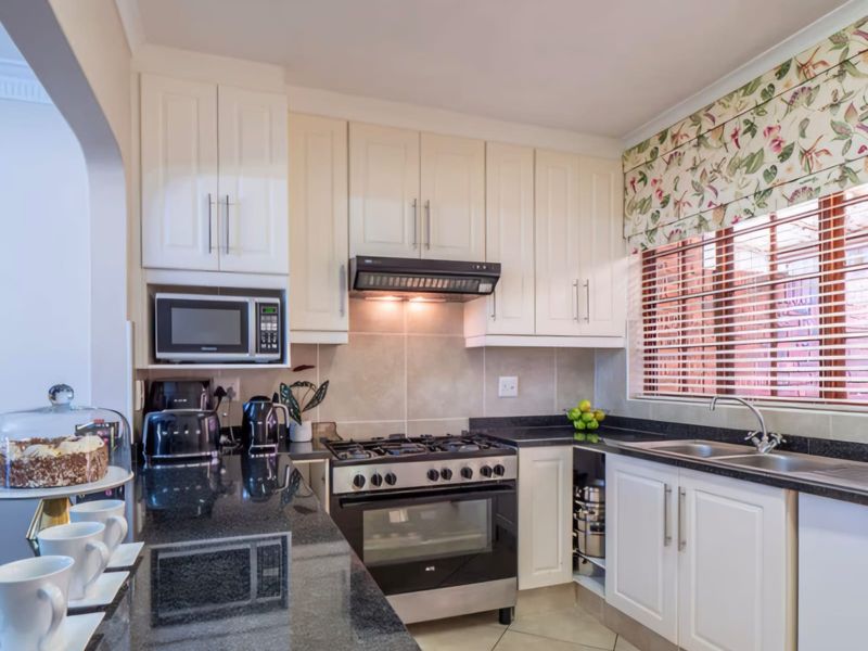 A well-maintained kitchen featuring granite countertops, ample cabinetry, a gas stove with extractor fan, and a double sink with natural light.