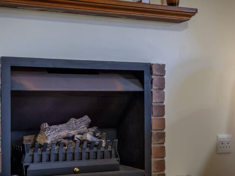 A close-up view of a built-in fireplace featuring a brick surround and a wooden mantelpiece in a living area.