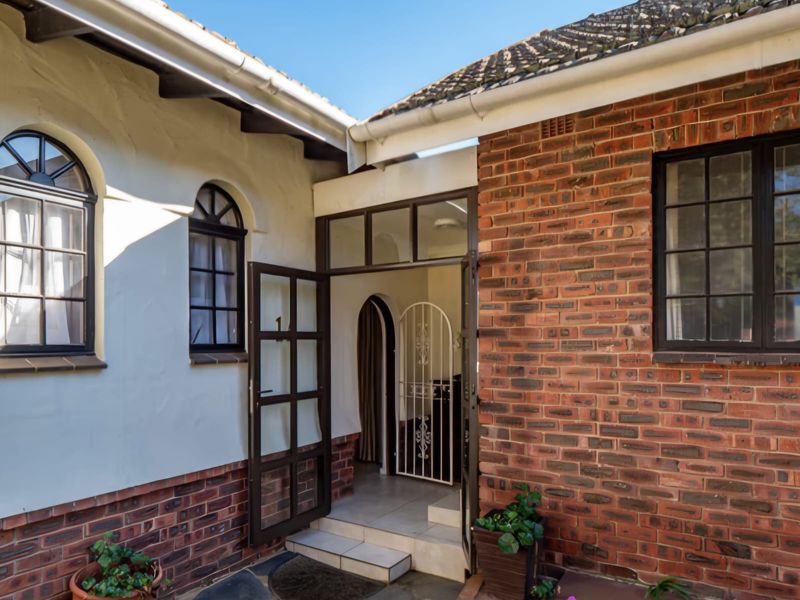 Entrance area featuring a combination of exposed brick and rendered walls, arched windows, and a secure gated doorway with tiled steps.