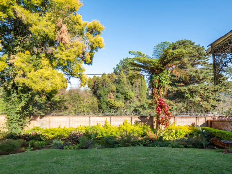 A well-maintained private garden featuring a lush lawn, mature trees, and a secure brick boundary wall with integrated security fencing.