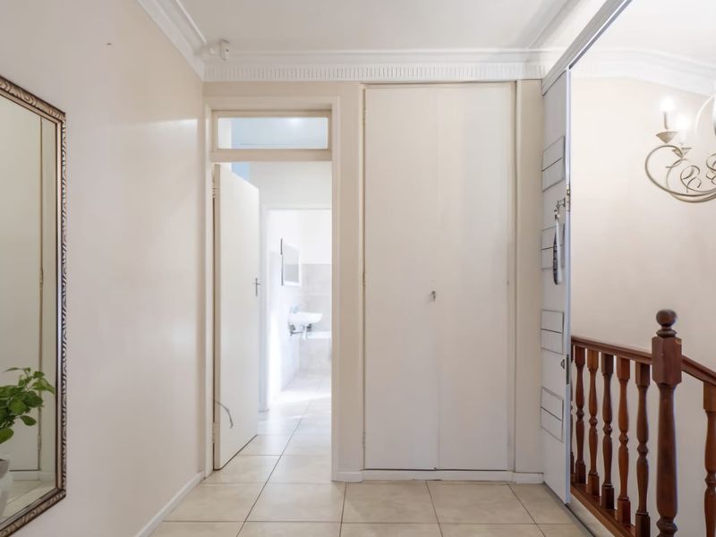 A bright, tiled hallway featuring a built-in cupboard, classic cornice detailing, and a wooden balustrade leading to an adjacent room.