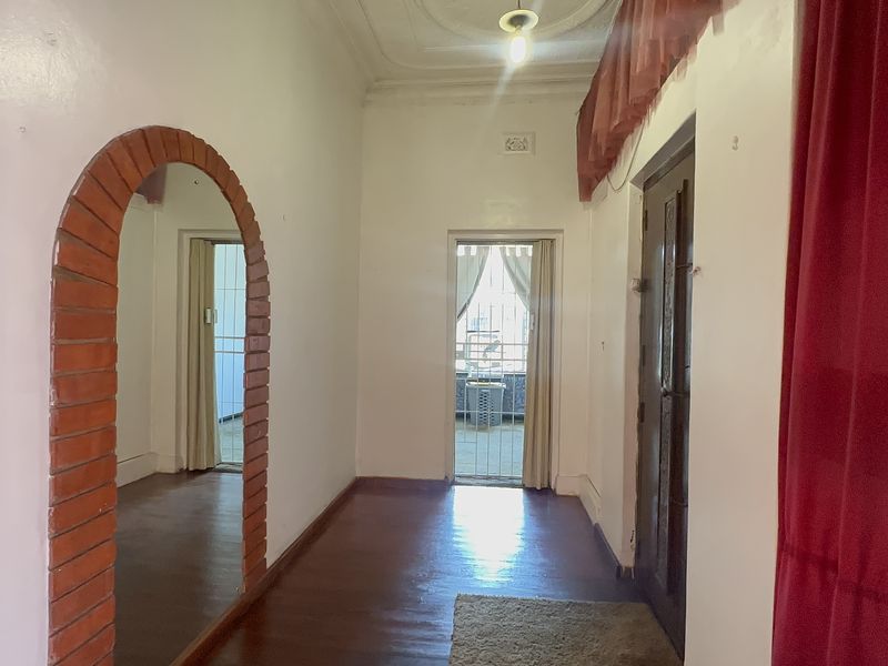 A spacious hallway featuring hardwood flooring, an ornate ceiling rose, and a distinctive arched brick doorway leading to an adjacent room.