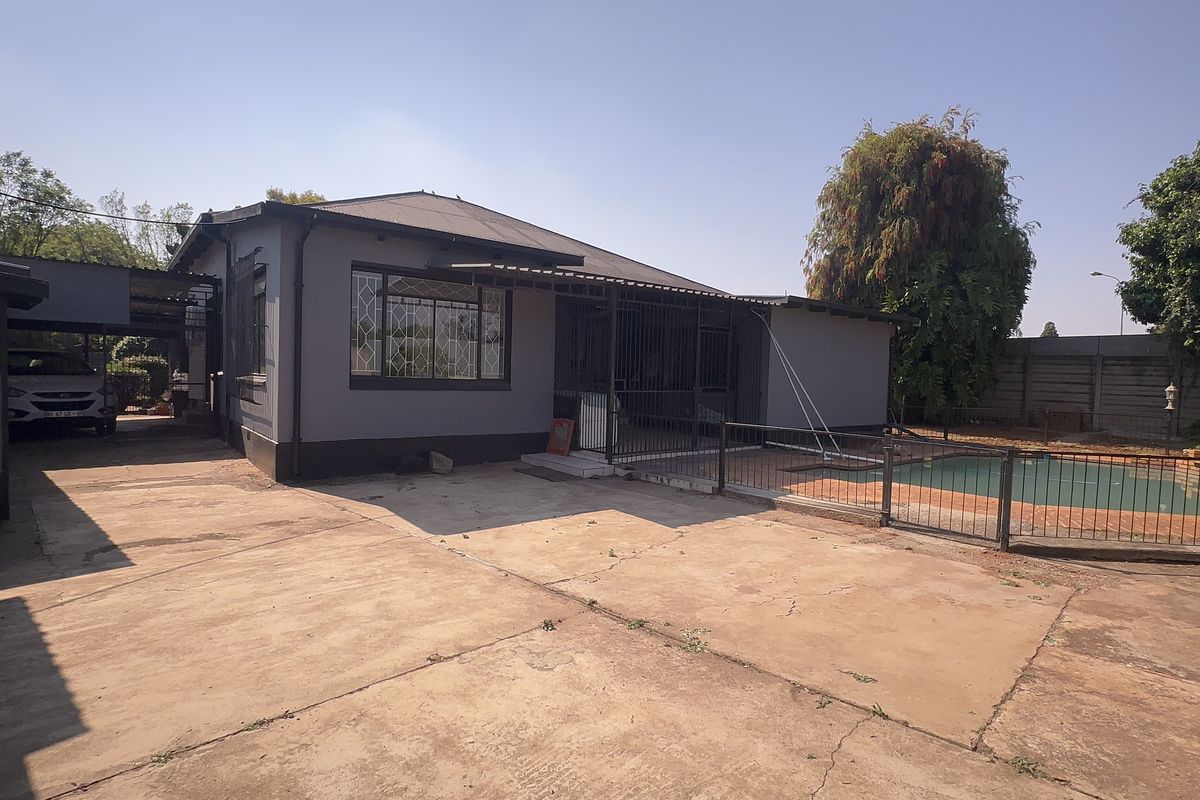 Rear view of the property featuring a swimming pool, paved driveway, carport, and secure perimeter fencing.