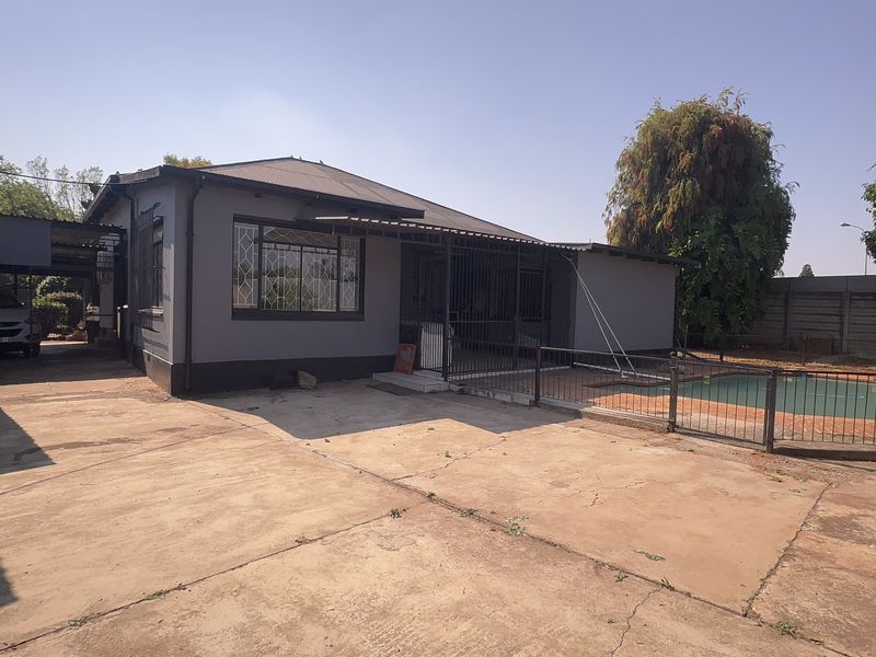 Rear view of the property featuring a swimming pool, paved driveway, carport, and secure perimeter fencing.