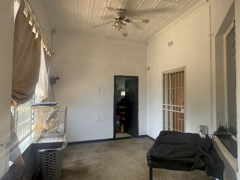 A living area featuring a classic pressed metal ceiling, ceiling fan, and security gate access, offering a blank canvas for renovation.