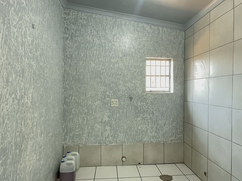 A vacant laundry room featuring tiled flooring, wall tiling, and dedicated plumbing connection points, requiring cosmetic updates to improve its overall condition.