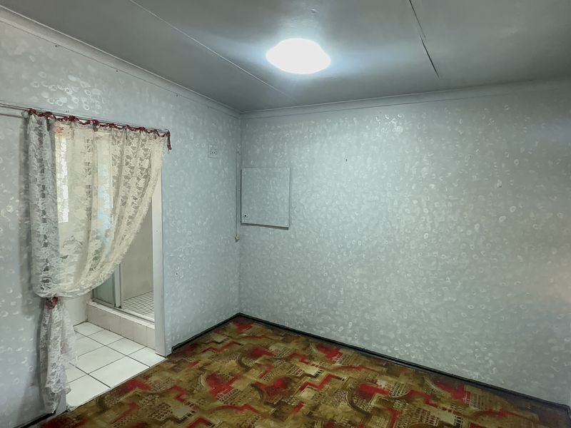An empty bedroom featuring patterned wallpaper and carpet, with direct access to an adjoining bathroom area.