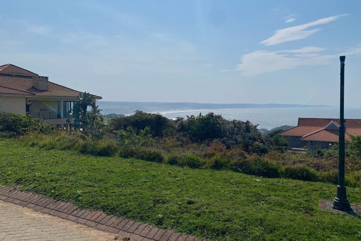 A scenic view overlooking the coastline and ocean from a residential property, featuring a paved driveway and landscaped surroundings.