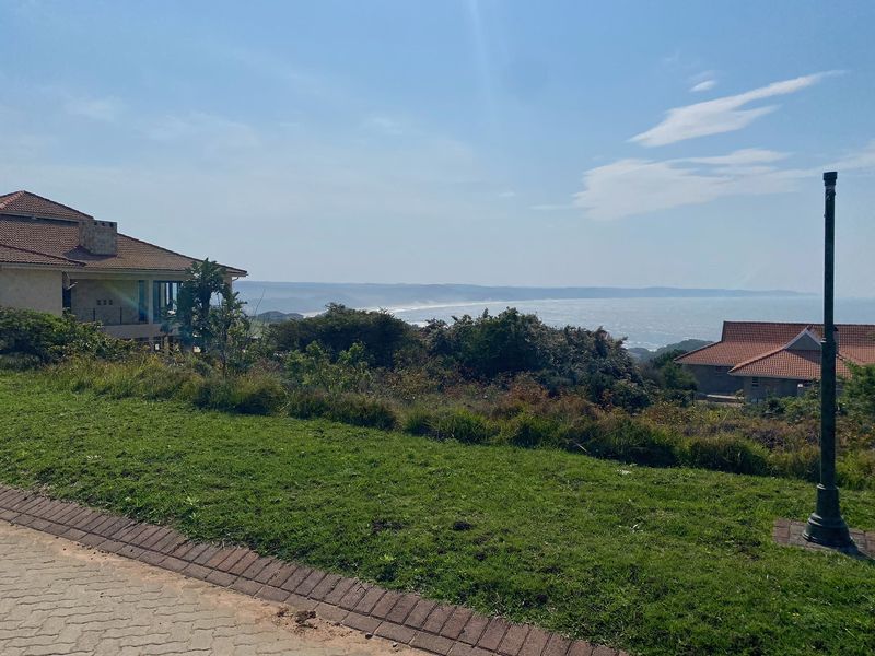 A scenic view overlooking the coastline and ocean from a residential property, featuring a paved driveway and landscaped surroundings.