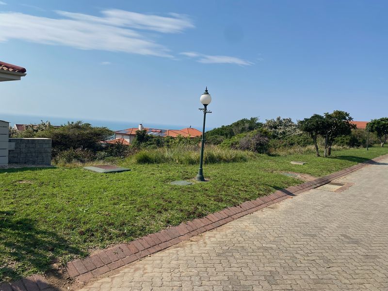 A view of the residential street frontage featuring a paved driveway, landscaped verge, and a decorative street lamp with distant coastal views.