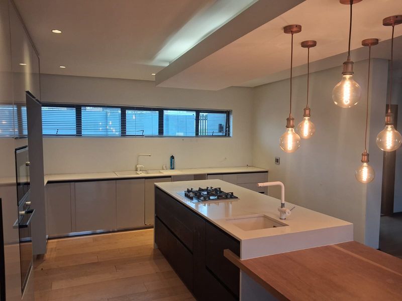 Modern kitchen featuring a central island with gas hob, stone countertops, integrated cabinetry, and stylish pendant lighting, set against light hardwood flooring.