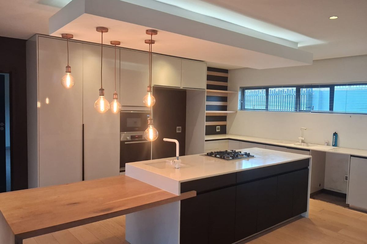 Modern, high-end kitchen featuring a large island with gas cooktop, integrated appliances, stone countertops, and stylish pendant lighting in a clean, contemporary space.