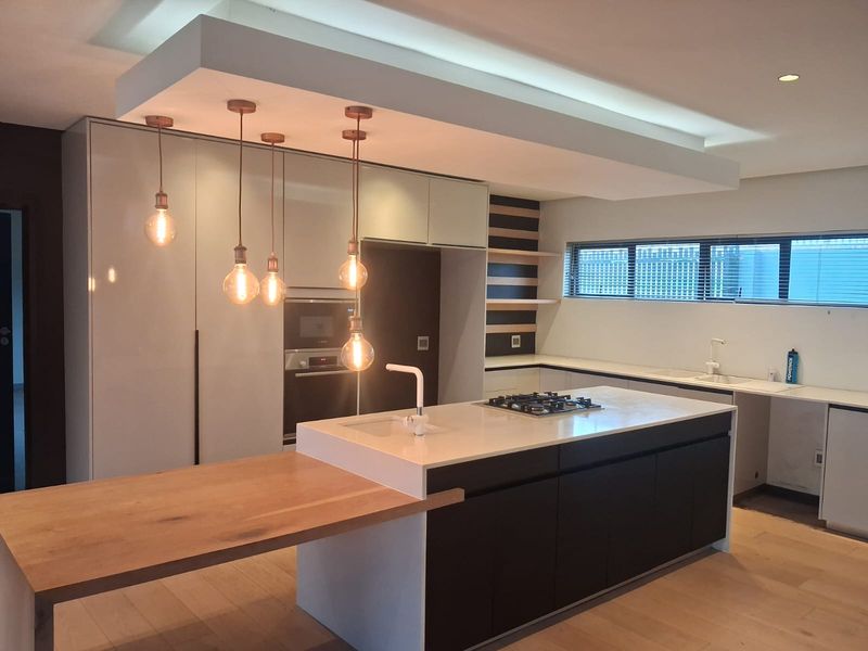 Modern, high-end kitchen featuring a large island with gas cooktop, integrated appliances, stone countertops, and stylish pendant lighting in a clean, contemporary space.