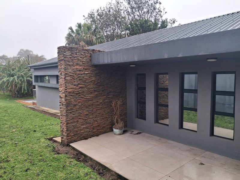 A covered patio area featuring modern stone cladding, tiled flooring, and large aluminium-framed windows overlooking the garden.
