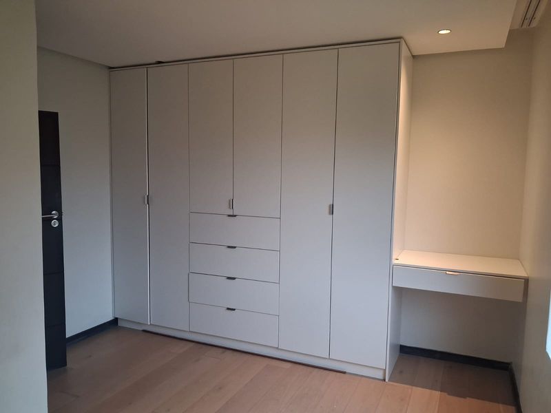 A clean, modern bedroom featuring extensive floor-to-ceiling built-in cabinetry with an integrated vanity desk and high-quality timber flooring.