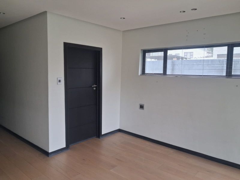 A clean, empty bedroom featuring modern timber flooring, recessed downlights, and contrasting black door and window frames.