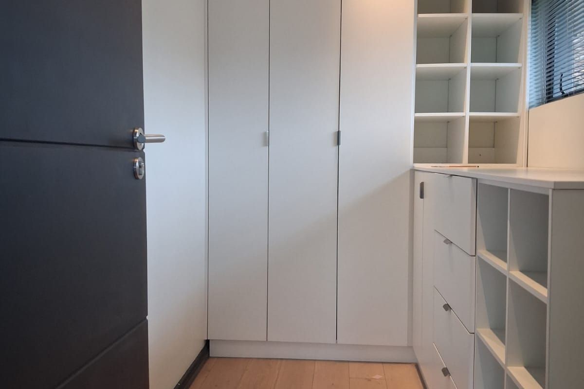 A clean, modern walk-in closet or dressing area featuring extensive built-in white cabinetry, shelving, and light timber flooring.