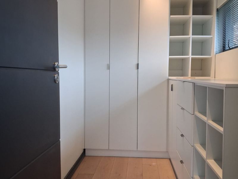 A clean, modern walk-in closet or dressing area featuring extensive built-in white cabinetry, shelving, and light timber flooring.