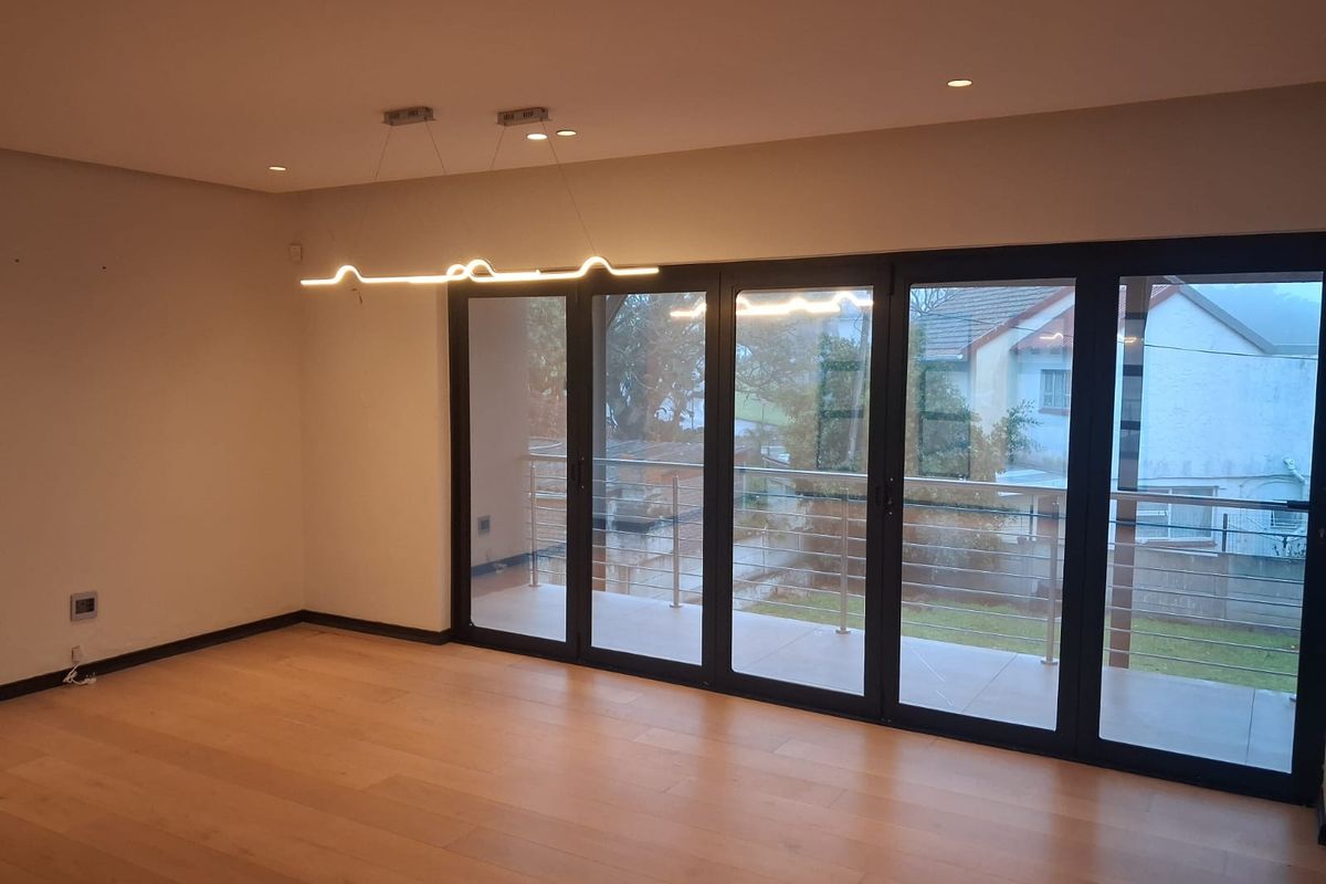 Spacious living area featuring light hardwood flooring, modern recessed and pendant lighting, and large aluminium stacker doors opening onto a private balcony.
