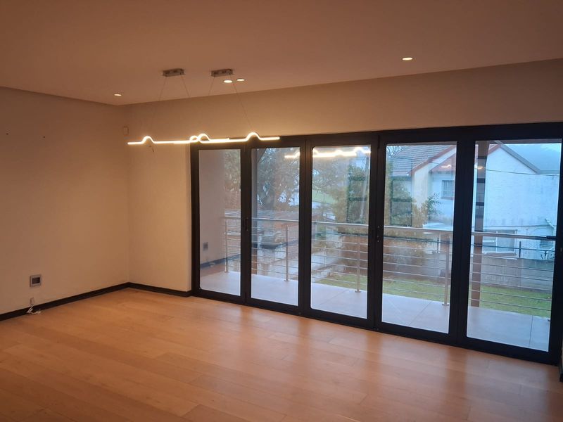Spacious living area featuring light hardwood flooring, modern recessed and pendant lighting, and large aluminium stacker doors opening onto a private balcony.