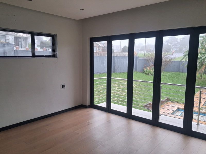 Bright and spacious living area featuring modern laminate flooring and large black aluminium stacker doors opening onto a garden and pool area.
