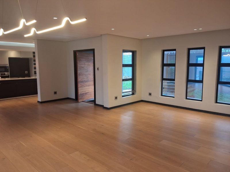 Spacious open-plan living area featuring high-quality hardwood flooring, modern lighting fixtures, and large aluminium-framed windows, providing a bright and contemporary atmosphere.