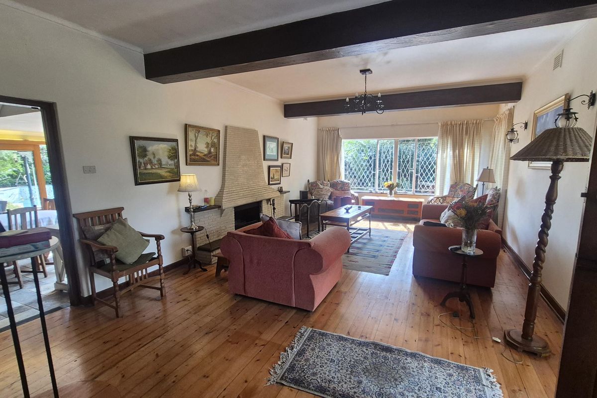 Spacious living room featuring exposed timber ceiling beams, a classic brick fireplace, and warm timber flooring with natural light through leaded glass windows.
