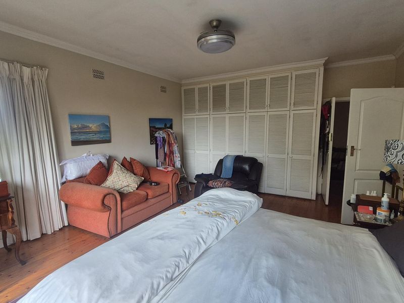 Spacious bedroom featuring hardwood flooring, extensive built-in cupboard storage, and a ceiling fan, offering a comfortable and functional living space.