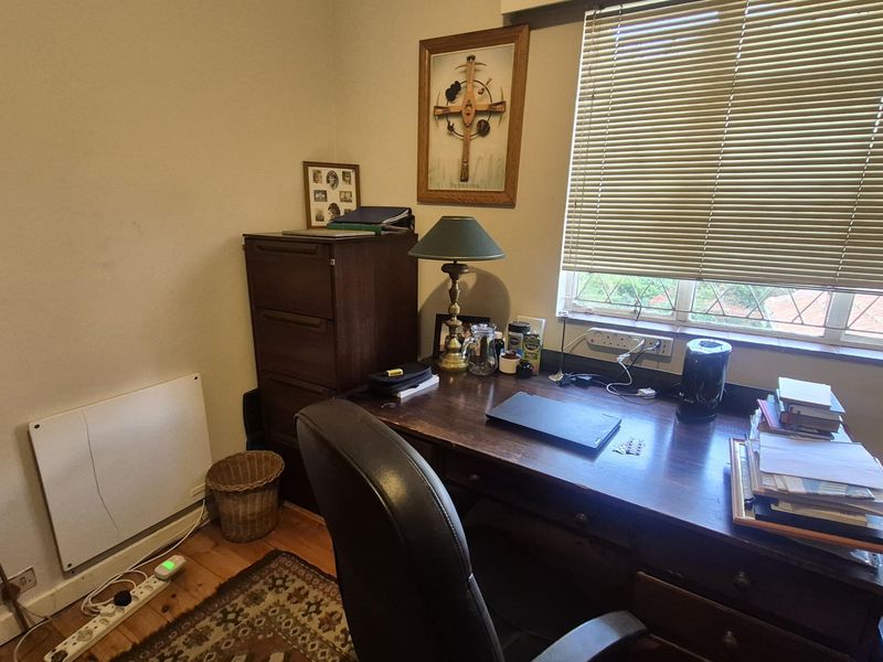 A functional home office space featuring timber flooring, a wall-mounted electric heater, and a window with venetian blinds.