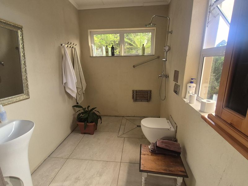 A functional bathroom featuring a pedestal basin, wall-hung toilet, and a walk-in shower area with tiled flooring and natural light.