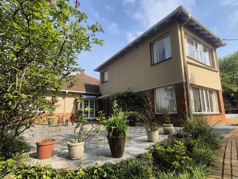 Rear view of the two-story house featuring a paved patio area, brick and plastered exterior walls, and established garden surroundings.