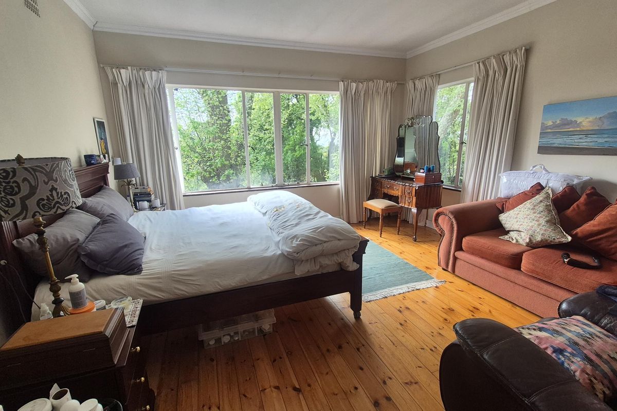 Spacious bedroom featuring polished timber flooring, large windows providing natural light and garden views, and classic cornice detailing.