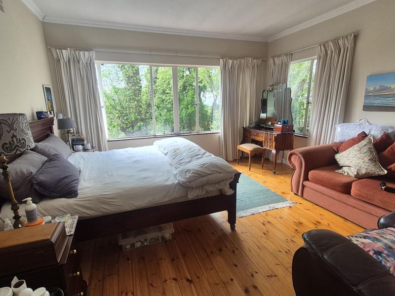 Spacious bedroom featuring polished timber flooring, large windows providing natural light and garden views, and classic cornice detailing.