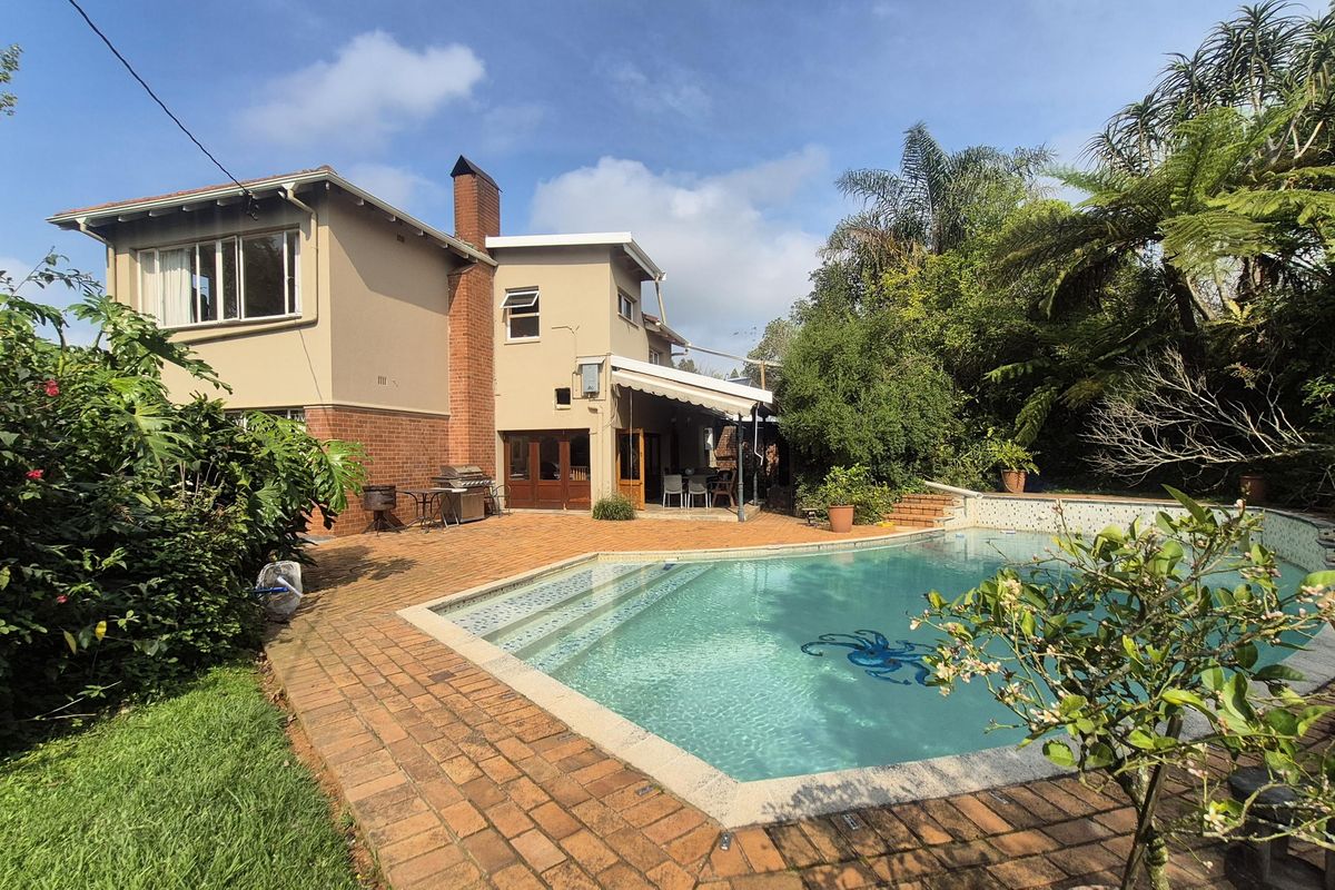 Rear view of the house featuring a swimming pool, brick paved patio area, and a retractable awning, set within a landscaped garden.
