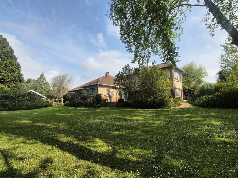 A view of the rear elevation of the house, featuring a large, well-maintained garden with mature trees and established landscaping.